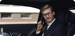 A man in a suit sits in the backseat of a car talking on his phone with a confident expression.