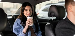 A young woman in casual wear enjoys a drink while seated comfortably in a chauffeured vehicle.