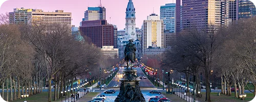 A central statue overlooks a wide avenue leading to City Hall, flanked by bare trees and tall buildings.