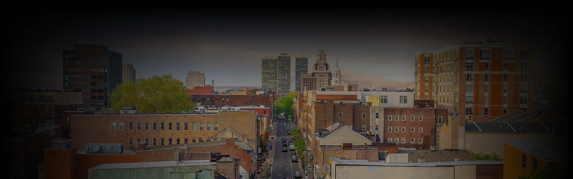 Philadelphia Car Service cityscape view featuring mid-rise brick buildings, tree-lined streets, and downtown skyscrapers captured from an elevated rear-angle perspective.